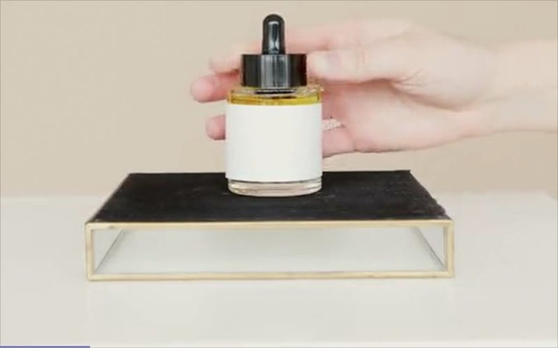A hand setting a dropper bottle of amber liquid with a blank white label onto a black tray